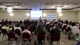 Wide shot of conference room with audience and speaker standing in front of a projection screen. 